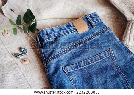 Trendy blue jeans, beige woolen sweater and earrings. Stylish winter outfit. Modern clothes for women flat lay photo