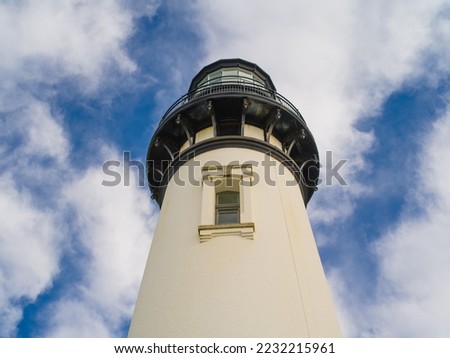 The white tower of a high lighthouse against a blue sky with white clouds. There is a small window on the tower. Beautiful design, great scenery. Travel destinations advertisement, banner, postcard.