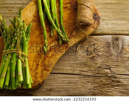 Green asparagus and a skein of twine on a cutting board on a wooden kitchen table. Close-up. Low angle view. Restaurant, hotel, home cooking, recipe book.
