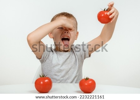 The boy don't like tomato. Nutrition and healthy eating habits for kids concept. Children do not like to eat red tomatoes. Little cute kid, boy refuse to eat healthy vegetables.