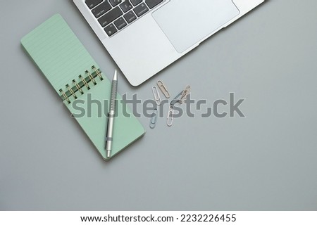 Small stylish green notepad and pen, laptop keyboard, paper clips, gray background. Concept of business, meeting preparation, time management, study online, web communication, connection. Copy space