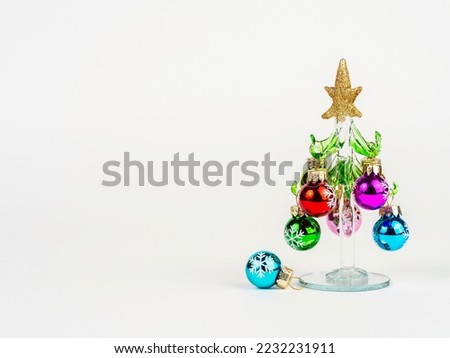 New Year's Eve photo with a glass Christmas tree, decorated with toys, standing on a white background. There is room for text.