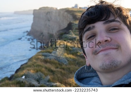 self portrait of a young adult on top of a cliff at sunset. Happy guy smiling and looking at camera. Mar del Plata cliffs.	
