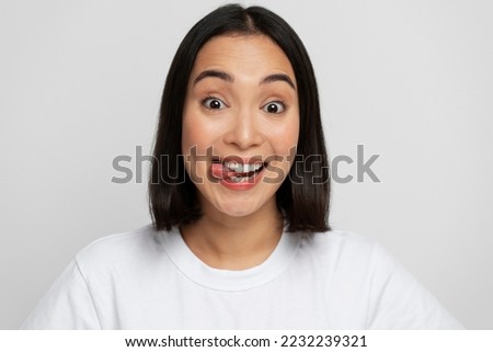 Portrait of positive playful woman standing with tongue out, demonstrating childish behaviour, wearing white T-shirt. Indoor studio shot isolated on white background 