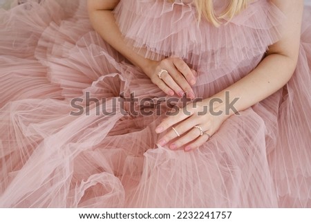 Beautiful female hands on a pink background of a puffy dress. Aesthetics of minimalism. The concept of spa, wedding salons, hand treatments