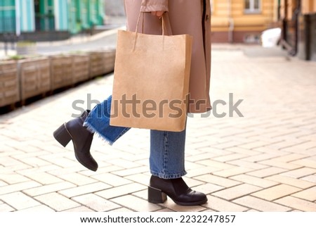 woman holding paper bag with place for text or logo in hands on city street. shopaholic content Royalty-Free Stock Photo #2232247857