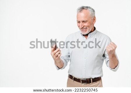 Caucasian happy as winner mature middle-aged grandfather using cellphone for lottery, online casino bets, cashback, sale discount offer isolated in white background Royalty-Free Stock Photo #2232250745