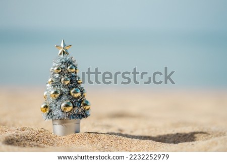 Sunshine day on the beach with a small Christmas tree in silver and gold decoration with blurry background, pastel tone, Christmas banner, happy concept
