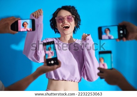 Teenage girl singing with people photographing her in smartphones Royalty-Free Stock Photo #2232253063