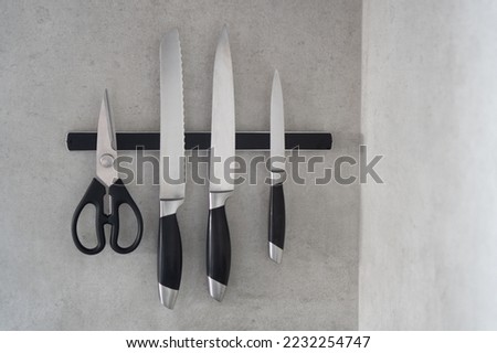 Magnetic knife holder. Magnetic bar for knives. Knives and scissors hang on a magnetic bar in the kitchen. Royalty-Free Stock Photo #2232254747