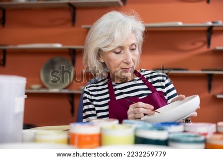 Mature craftswoman painting a clay plates acrylic paints in art studio