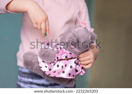 Little girl is vaccinating a teddy bear. 