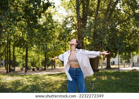 Carefree asian girl dancing, feeling happiness and joy, enjoying the sun on summer day, walking in park with green trees. Royalty-Free Stock Photo #2232272349