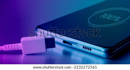 Fully charged battery. A 100 percent icon on the touch screen of the cell phone and a USB Type-C cable. Fully charged smartphone battery. Keeping the battery intact Royalty-Free Stock Photo #2232272565