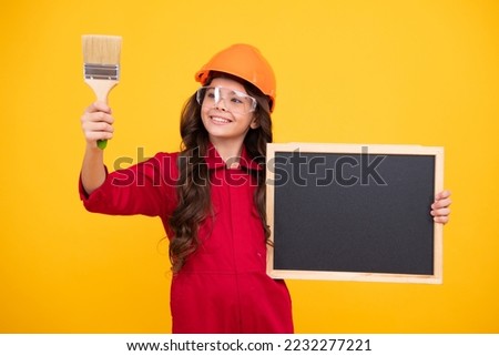 Teenager child painter in helmet with painting brush. Child in hard hat. Kid builder painter on construction site. Renovation and repair. Happy smiling emotions of teenager girl.