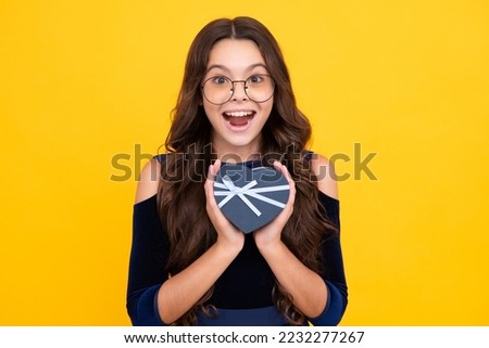Excited teenager girl. Teenage child holding gift box on yellow isolated background. Gift for kids birthday. Christmas or New Year present box.