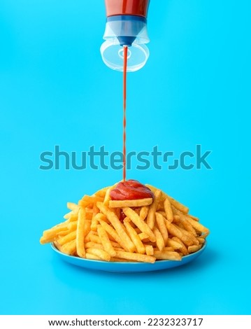 Pouring ketchup from a bottle over french fries, minimalist on a blue background. Delicious meal, french fries with ketchup in bright light on a colorful table.