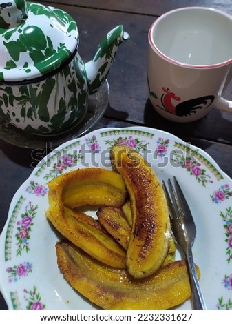 Fried bananas without toppings placed on a legendary white plate. Combined with hot and strong tea. Also the legendary mug with a picture of chicken.