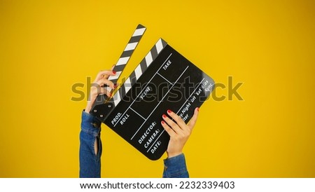 Hand is holding clapper board or clapperboard or movie slate, used in film production and cinema ,movies industry isolated over yellow background. Royalty-Free Stock Photo #2232339403