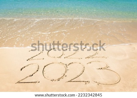End of 2022 Happy New Year 2023, lettering on sunrise beach with wave and foam bubble in the morning. Handwritten inscription 2022 and 2023 on beautiful sand beach. New Year 2023 replace 2022 concept.
