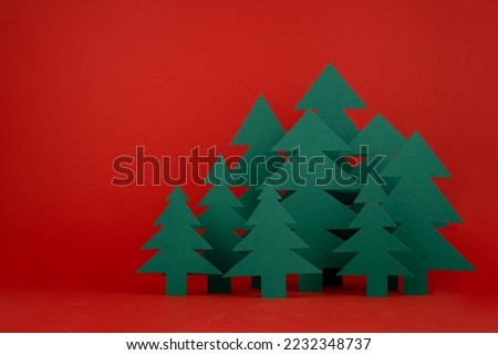 Bright Christmas background with paper green spruce forest on red backdrop in minimalist modern style, copy space. New year scene for presentation products and advertising text, card, poster, flyer.