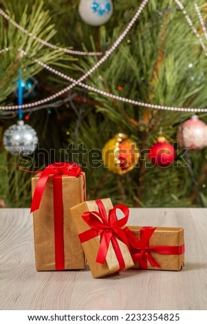 Gift boxes with red bows. Christmas tree with blurred twinkling party lights and toy balls on the background. Christmastime celebration.