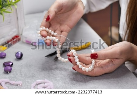 Close hand jeweler stringing pearls on a necklace