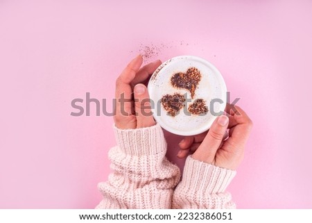 Cup with coffee latte with heart decoration. Heart Shape Coffee Art on coffee or hot chocolate drink, in woman hands on pink background. Valentine day, birthday, woman day greeting card background
