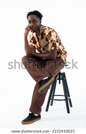 Stylish man with adorable funny hairstyle sitting on chair isolated in white studio looking at camera posing.