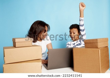 Portrait of excited woman and teen boy doing online order on laptop over blue background. Looking happy. Concept of shopping, online order and delivery, Black Friday sales. Copy space for ad, text