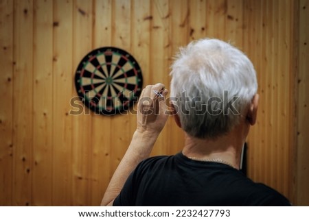 A man with gray hair plays darts. Rear View Of Man Playing Darts.