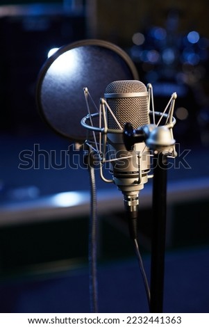 Microphone with a pop shield closeup on the background of a professional recording studio. Microphone stand with a condenser for records vocals, speakers and sound of musical instrument. 