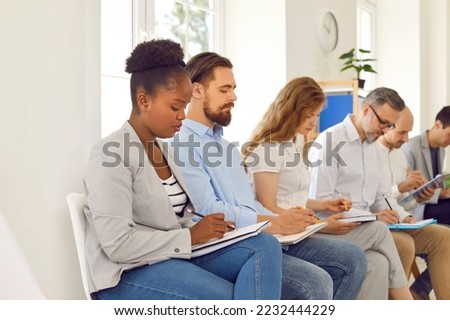 People take notes at business conference. Multiracial male female audience sitting in line in office room, listening to lecture and writing down information on clip boards, notepads, folders, binders Royalty-Free Stock Photo #2232444229