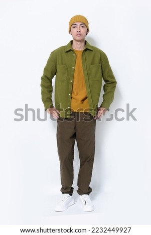 a handsome attractive full body young man in a green shirt sweater ,brown pants with hat stands in studio