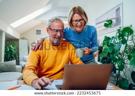 Happy senior couple reading good news on a laptop at home and using internet together. Smiling elderly spouses reading a mail, checking paying bills online, discussing budget planning. Royalty-Free Stock Photo #2232453675