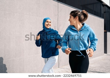 Cheerful muslim woman wearing hijab running in the street with her friend and having fun. Royalty-Free Stock Photo #2232469751