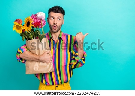Photo of impressed handsome guy hold bunch flowers bag look direct finger empty space isolated on turquoise color background
