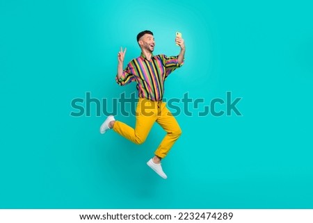 Full body photo of funny jumping air guy wear striped shirt showing v-sign selfie with smartphone hello followers isolated on cyan color background