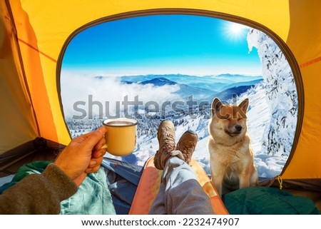 Cup of hot drink in the hand  and wonderful view of snowy mountain tops through the open entrance to the tent. The beauty of a romantic hike and camping accompanied by a dog.