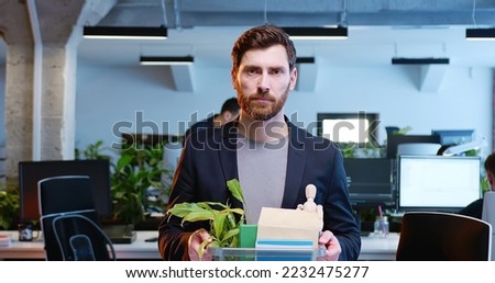 Portrait of sad Caucasian male emloyee fired from work. Upset young man with box full of things and stuff in hands looking at camera. Coworking space. Firing from job. Dismissing. Royalty-Free Stock Photo #2232475277