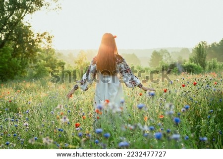 Woman with poppy in hair scenic photography. Blossoming field. Picture of lady with beautiful wildflowers on foreground. High quality wallpaper. Photo concept for ads, travel blog, magazine, article