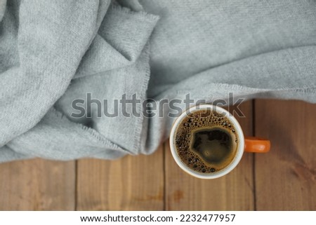 Top view of orange Cup of hot coffee Warm grey scarf a on wooden table. Good morning. Winter mood concept. Warm autumn or winter picture. Time for relax. Coffee Love