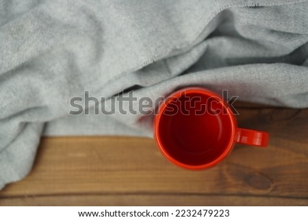 Top view of red Cup. Warm grey scarf a on wooden table. Good morning. Winter mood concept. Warm autumn or winter picture. Time for relax. 