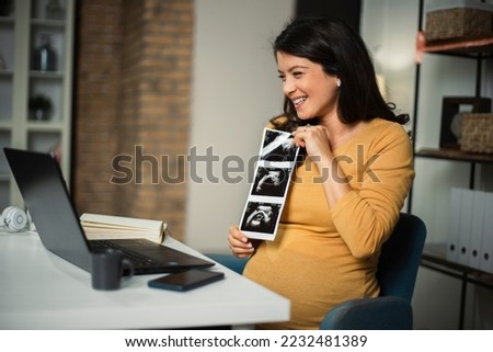 Beautiful young pregnant woman looking at ultrasound pictures of her baby. Businesswoman having video call