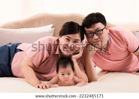 Happy asian family laying down and taking pictures together in bedroom. parents and little daughter looking at camera posing for photo. Exemplary family portrait, love and bond concept