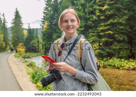 Travel at mountains. Young woman traveler with backpack holding smartphone device in hands. Autumn hike in the forest. Adventures in nature. Active lifestyle