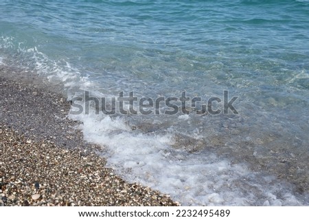 Bank of pebbles with the sea and beach in the background. Pebbles and water on the sea shore in Kemer, Antalya in Turkey
