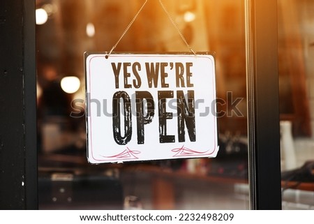 Inscription Yes we're open metal plate with black and white sign on glass door store, cafe, beautystore, barbershop after coronavirus lockdown quarantine. business reopen again.