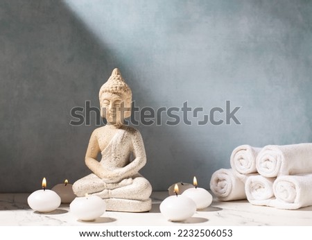  Spa setting. Buddha and burning small white candles against blue textured wall. Wellbeing time concept. Place for text.