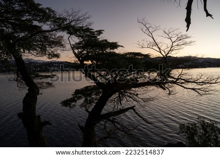 Magical view of the dark silhouette of the forest trees, calm lake and mountains, under a nightfall sky.  Royalty-Free Stock Photo #2232514837
